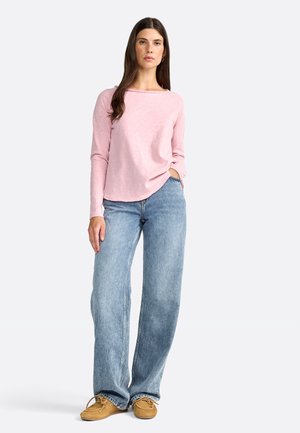 Top de manga larga color rosa claro con un dobladillo redondeado, combinado con jeans de mezclilla azul deslavado de pierna ancha y zapatos marrón claro.