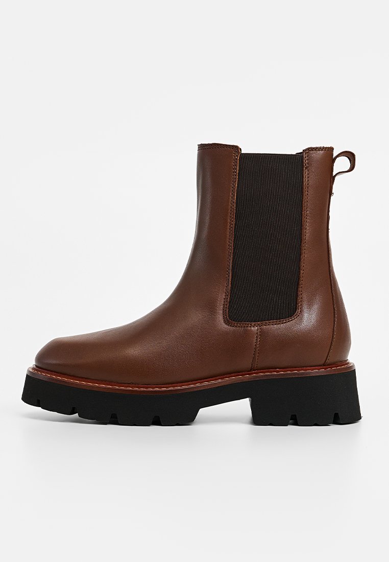 Braune Leder-Stiefelette mit elastischen seitlichen Einsätzen, abgerundeter Zehenpartie und einer dicken schwarzen Gummisohle. Sichtbare Steppnähte entlang der Kante.