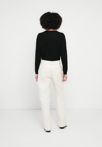 Fekete hosszú ujjú felső, krémszínű, texturált, széles szárú nadrággal párosítva, amely övhurkokkal és oldalzsebekkel rendelkezik. A ruházat testre szabott és szabott.