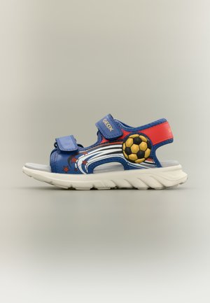 Blue and red children’s sandal with white sole, Velcro straps, star and soccer ball designs, and brand name Geox on straps.