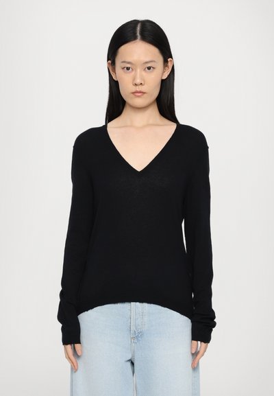 Pull noir en V en tissu doux, avec des manches longues et une coupe décontractée, associé à un jean taille haute bleu clair.