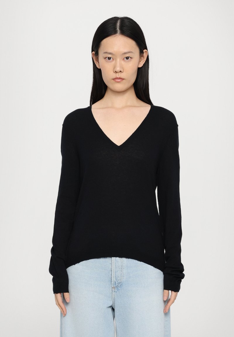 Zwarte V-hals trui van zacht materiaal, met lange mouwen en een relaxte pasvorm, gecombineerd met lichtblauwe high-waisted jeans.