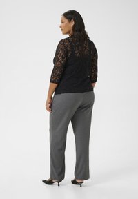 Un haut en dentelle noire avec des manches 3/4, associé à un pantalon gris clair. La tenue présente une coupe ajustée et une texture subtile. Des talons noirs complètent le look.