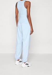 Person som står med ryggen mot kameran, iklädd en ljusblå ärmlös topp, matchande joggingsbyxor och vita sneakers med svarta ränder.