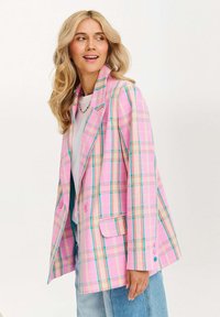 Ružový károvaný blejzer s modrými a žltými akcentmi, jednoradový dizajn, dve gombíky a so špicatým golierom. Štylizované s džínsami.