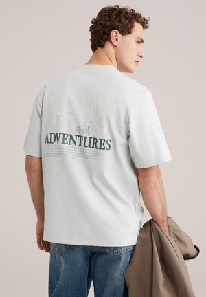 Lichtgrijs T-shirt met korte mouwen, voorzien van een bloemenafbeelding en tekst op de achterkant. Heeft een losse pasvorm en een gladde stoftextuur.