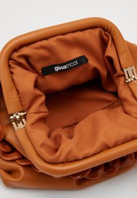 Borsa in pelle sintetica marrone con un interno morbido in tessuto. Presenta hardware dorato, bordi arrotondati e un'etichetta con il marchio all'interno.