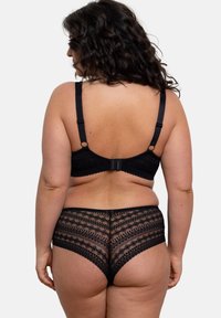 Soutien-gorge en dentelle noire et culottes assorties, avec des motifs géométriques et des bords festonnés. Bretelles réglables et fermeture à crochet au dos.