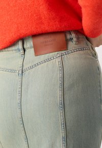 Lyseblå denimjeans med høy midje, med kontrasterende sømmer og en brun lærmerkelapp bak.
