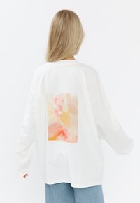 Biała, oversize'owa bluza z haftem w kształcie prostokąta w stylu akwareli, w delikatnych odcieniach różu, pomarańczy i żółci na plecach.