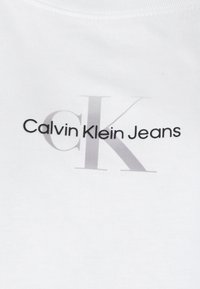Biała bawełniana koszulka z nadrukiem "Calvin Klein Jeans", z wyraźnym szarym logo "CK". Prosty, minimalistyczny design.