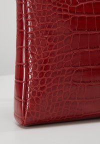 Rød taske med krokodillepræg og blank finish, der har en struktureret form og tekstureret overflade.