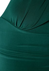 Gros plan d'un tissu de robe vert, présentant une texture lisse et extensible avec des fronces au niveau de la poitrine et des coutures horizontales. Fini avec un doux éclat.