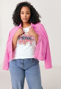 Rosa strukturierte Jacke über einem weißen T-Shirt mit einem bunten "SPRING"-Grafik. Kombiniert mit hellblauen weit geschnittenen Jeans.