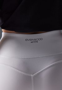 Valkoiset korkeavyötäröiset legginsit, joissa on sileä pinta, ja vyötäröllä on "even&odd ACTIVE" -logo sekä kontrastiväriset ompeluyksityiskohdat.