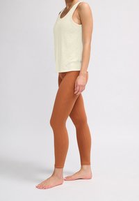 Ljusbeige linne med en strukturerad finish, kombinerat med figurnära, randiga bruna leggings. Modellen står barfota och visar upp outfiten.