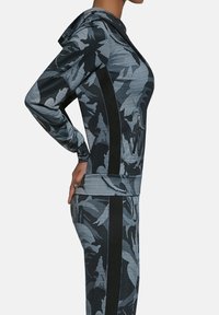 Czarna i szara sportowa kurtka z kapturem w kamuflażowy wzór, wyposażona w teksturowane panele, kieszenie na zamek oraz dopasowany krój.