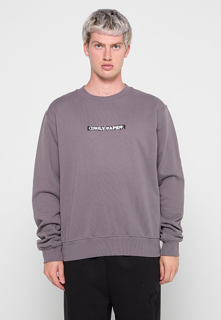 Grauer Pullover aus weichem Material mit rundem Halsausschnitt und langen Ärmeln. "DAILY PAPER"-Logo in Schwarz und Weiß auf der Brust gestickt.