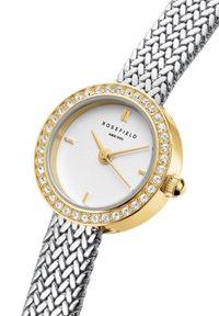 Montre ronde dorée avec un bracelet en maille argentée, cadran blanc et accents en cristal sur la lunette. Présente des marqueurs d'heure simples et une couronne.