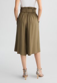 Culotte verde oliva con gamba ampia, vita elasticizzata e tasche laterali. Abbinati a tacchi in stampa pitone con tacco a blocco.