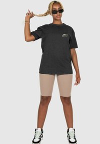 Black oversized cotton t-shirt with a small logo on the chest, beige bike shorts, and black sneakers with white accents.