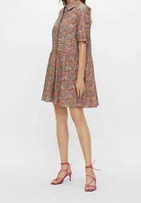 Krótka sukienka w kwiaty z krótkim rękawem, kołnierzykiem, wielowarstwowymi spódnicami i wielokolorowymi wzorami. Uzupełniona o różowe sandały na paski.