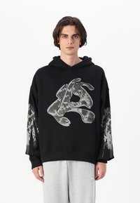 Svart hettegenser med stort grått grafisk motiv på fronten og et teksturert mønster på ermene. Sammen med grå joggebukser.
