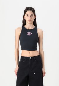 Black cropped tank top with ribbed texture, featuring pink embroidered "OBEY" logo at center. Paired with black baggy trousers.