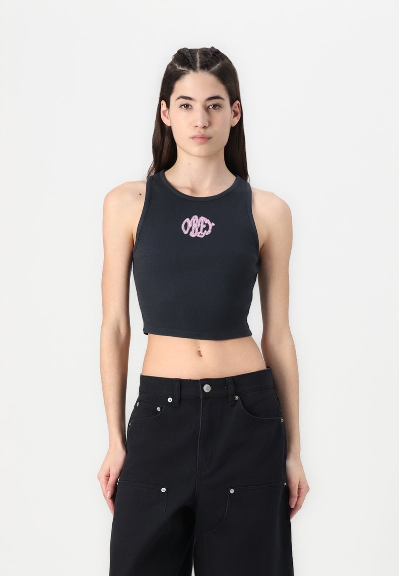 Black cropped tank top with ribbed texture, featuring pink embroidered "OBEY" logo at center. Paired with black baggy trousers.