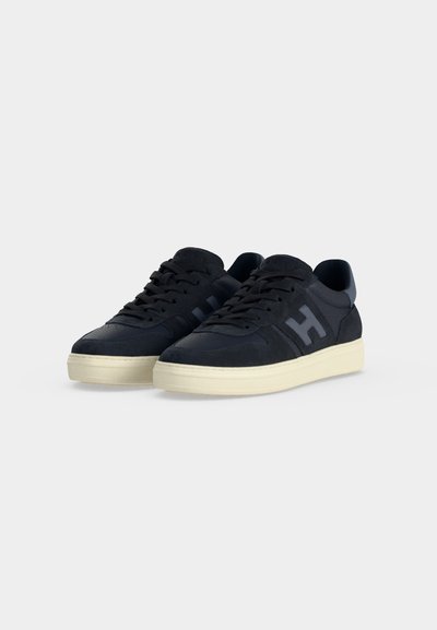 Ζευγάρι μαύρα sneakers χαμηλού τύπου με λευκές σόλες και κορδόνια, με μεγάλο λογότυπο H στο πλάι.
