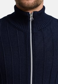 Dunkelblauer gestrickter Pullover mit geripptem Muster, hohem Kragen und silbernem Reißverschluss. Verfügt über vertikale Linien im gesamten Stoff.