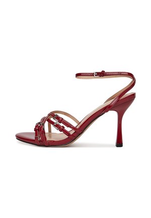 Sandalia de tacón alto de charol rojo con múltiples tiras cruzadas y una correa en el tobillo con hebilla metálica. Acabado liso y brillante.