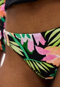 Κοντινό πλάνο της μέσης που φορά μαγιό με τροπικά λουλούδια σε πράσινο, ροζ, πορτοκαλί και μαύρο χρώμα.