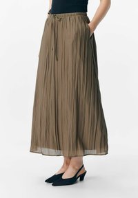 Falda larga plisada en verde oliva con cinturilla elástica y cordón ajustable. Lleva consigo unos zapatos de tacón negro tipo slingback, con punta afilada.