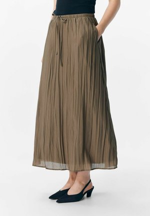 Plisseret, lang nederdel i oliven grøn med elastisk talje og snøre. Bæres med sorte slingback hæle, der har spids tå.