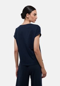 T-shirt en coton bleu marine avec des manches courtes roulées et une coupe décontractée. Présente un col rond et un ourlet droit, texture lisse.