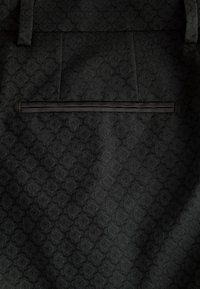 Tessuto nero a motivo con un sottile design geometrico. Presenta una tasca piatta con un orlo nero a contrasto. Texture morbida, aspetto strutturato.