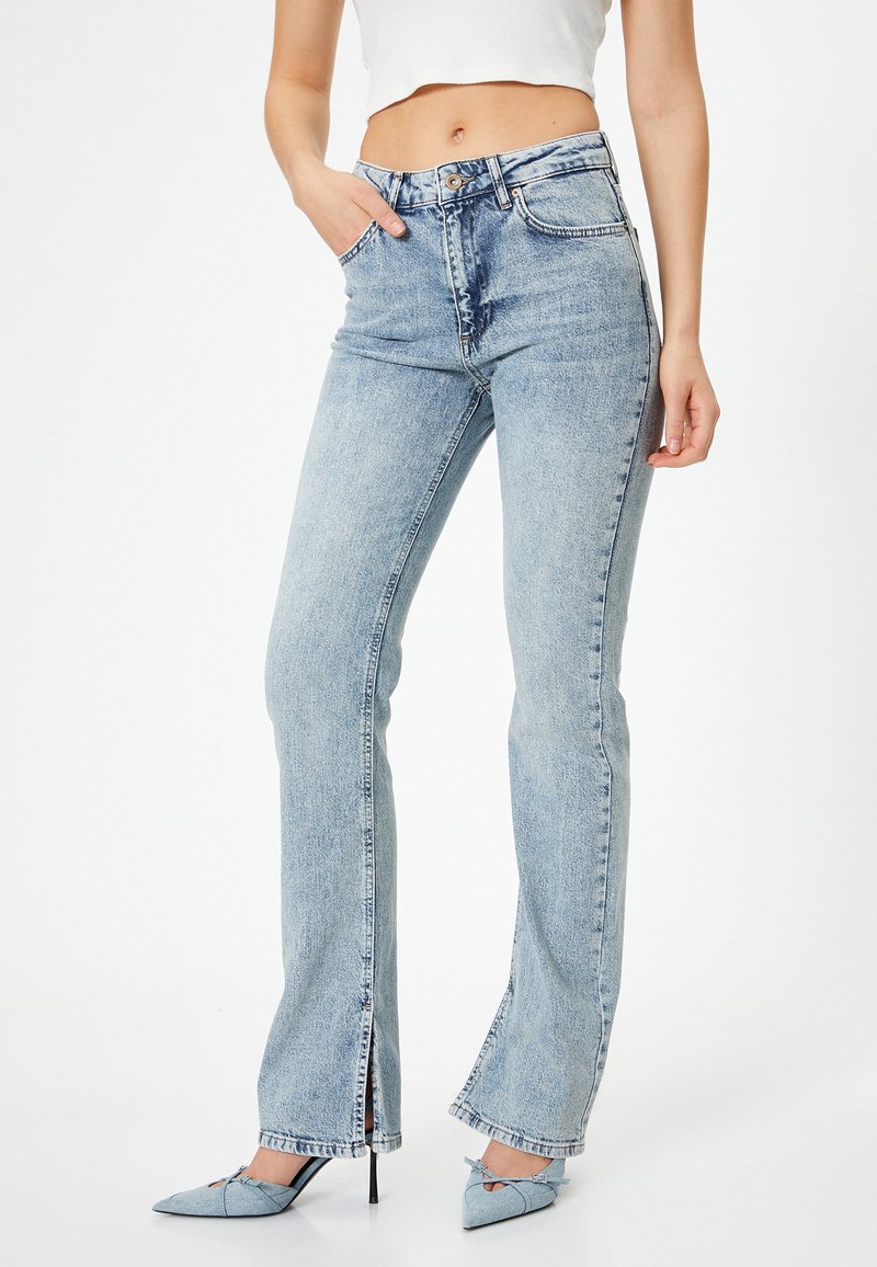Pantalones vaqueros de mezclilla azul claro, acampanados, con cintura alta, bolsillos delanteros y aberturas en los laterales del dobladillo. Textura suave, diseño casual.