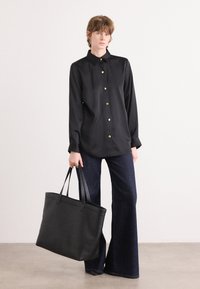 Camisa preta de botão com colarinho, apresentando botões dourados. Combinada com jeans escuros flare e uma grande bolsa tote preta com alças resistentes.
