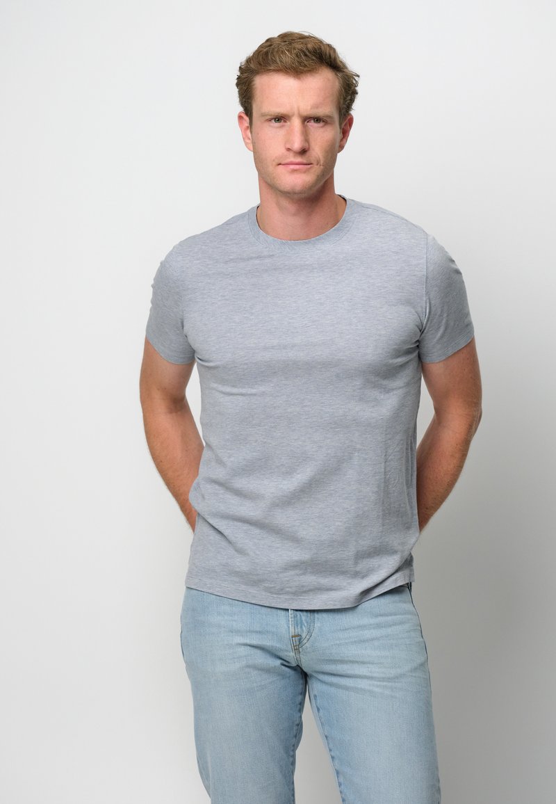 Grå bomullströja med kort ärm och rund halsringning, med en slät yta och en figurnära design. Buren med ljusblå jeans.