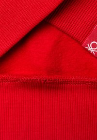 Textil rojo con un exterior acanalado y un interior suave y cepillado. El borde muestra una puntada en zigzag con una pequeña etiqueta. Color rico y uniforme en toda la superficie.