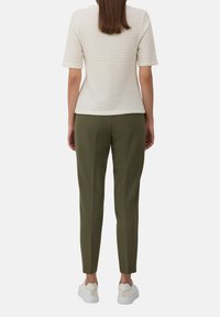 Haut crème texturé à manches courtes associé à un pantalon tapered vert olive et des baskets blanches. Dans l'ensemble, une silhouette à la fois épurée et moderne.