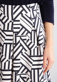 Woman's hand beside white skirt with black geometric stripe pattern, wearing a long-sleeve dark navy top.