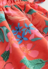 Vestido floral con una vibrante tela roja adornada con patrones de flores azules, rosas y verdes. La textura es suave y está fruncido en la cintura.