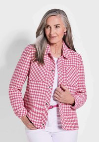 Rosa-weiße Hahnentwistjacke mit Kragen, vorderen Taschen und silbernen Druckknöpfen; über einem weißen Oberteil getragen und mit einem rosa Gürtel kombiniert.