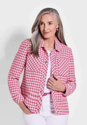 Roze en witte houndstooth jas met een kraag, voorzakken en zilveren drukknoopsluitingen; gedragen over een witte top en gecombineerd met een roze riem.