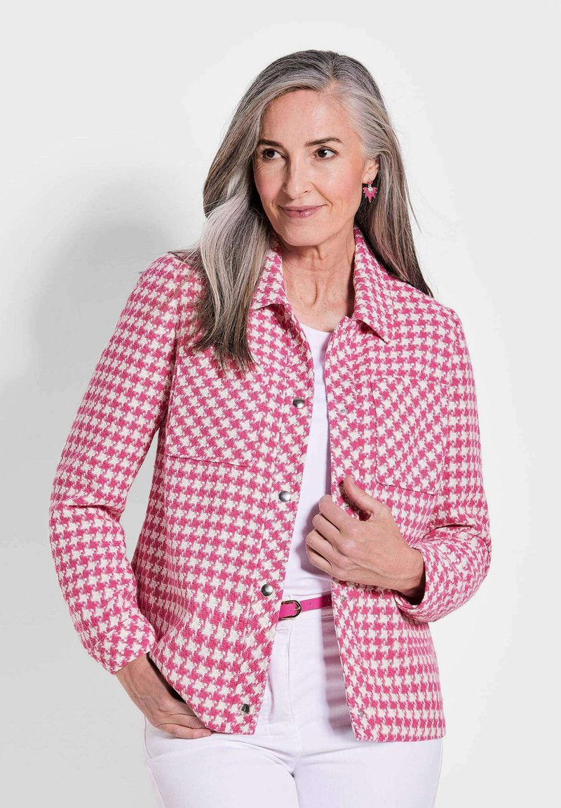 Rosa-weiße Hahnentwistjacke mit Kragen, vorderen Taschen und silbernen Druckknöpfen; �über einem weißen Oberteil getragen und mit einem rosa Gürtel kombiniert.