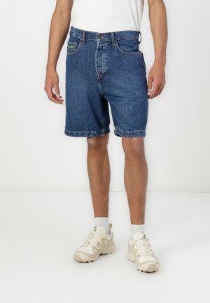 Denim shorts, blue, with a traditional five-pocket design and visible stitching. Features a regular fit and frayed hem. Worn with beige sneakers.