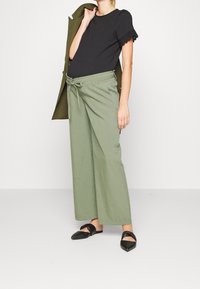 Svart t-shirt med spetsdetaljer på ärmarna, parat med löst sittande olivgröna byxor med dragsko i midjan, och svarta spetsiga flats.