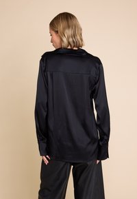 Svart satin skjorte med ryggpanel, lange ermer og knappebeslag detaljer. Jevn tekstur med klassisk krage og flytende design.